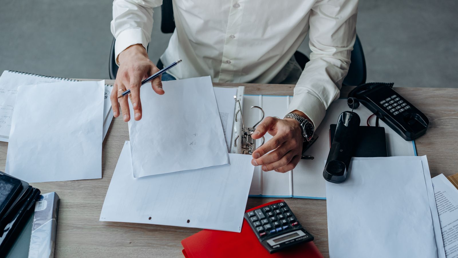 A business professional organizing documents at a busy office desk.