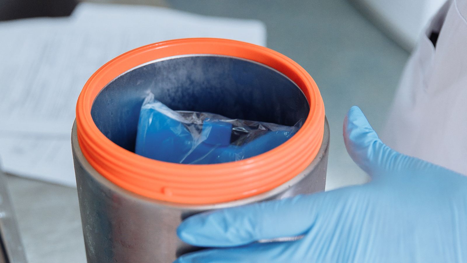 A gloved scientist opens a sterile container inside a laboratory.