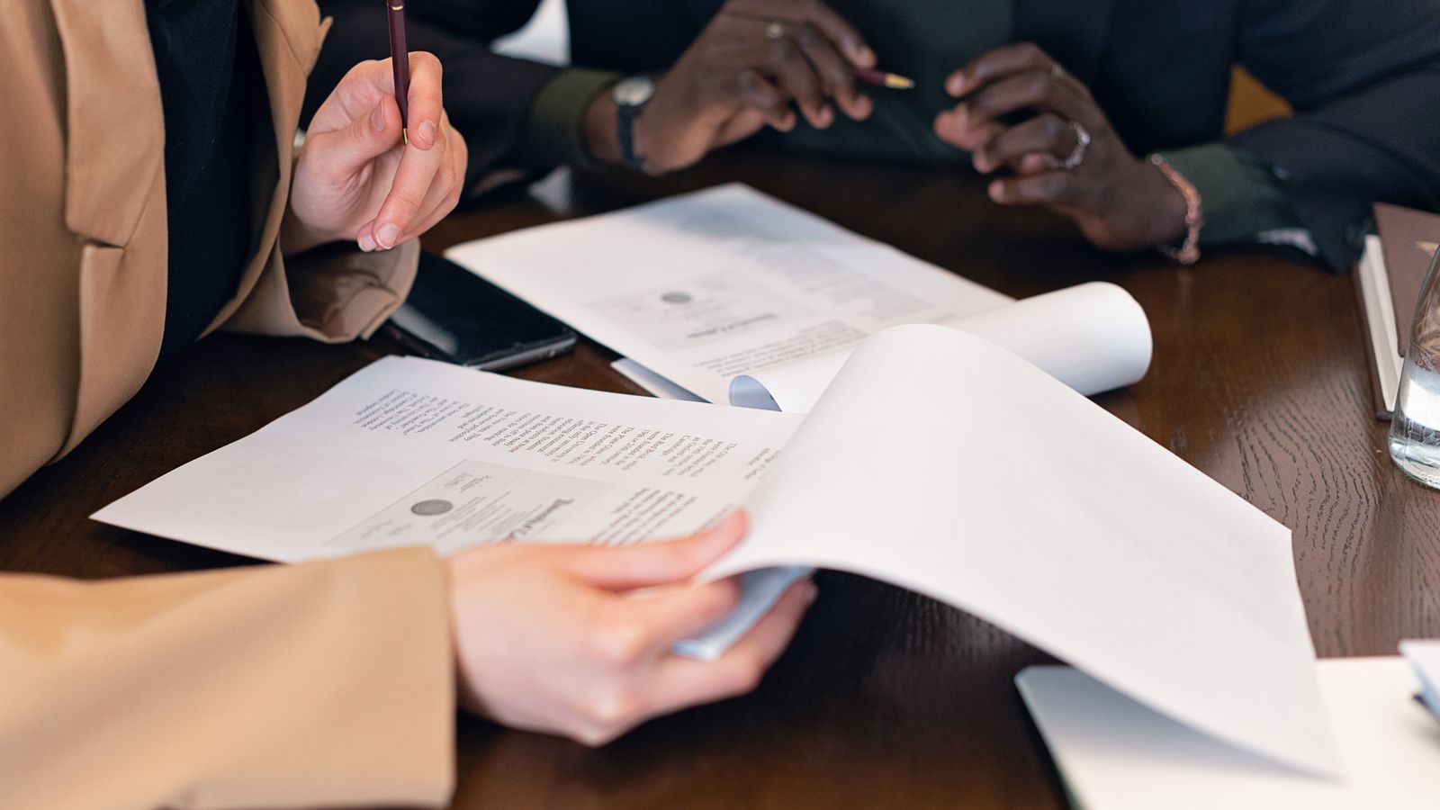 Two colleagues in business attire lean over a table, reviewing printed documents together during an office meeting.