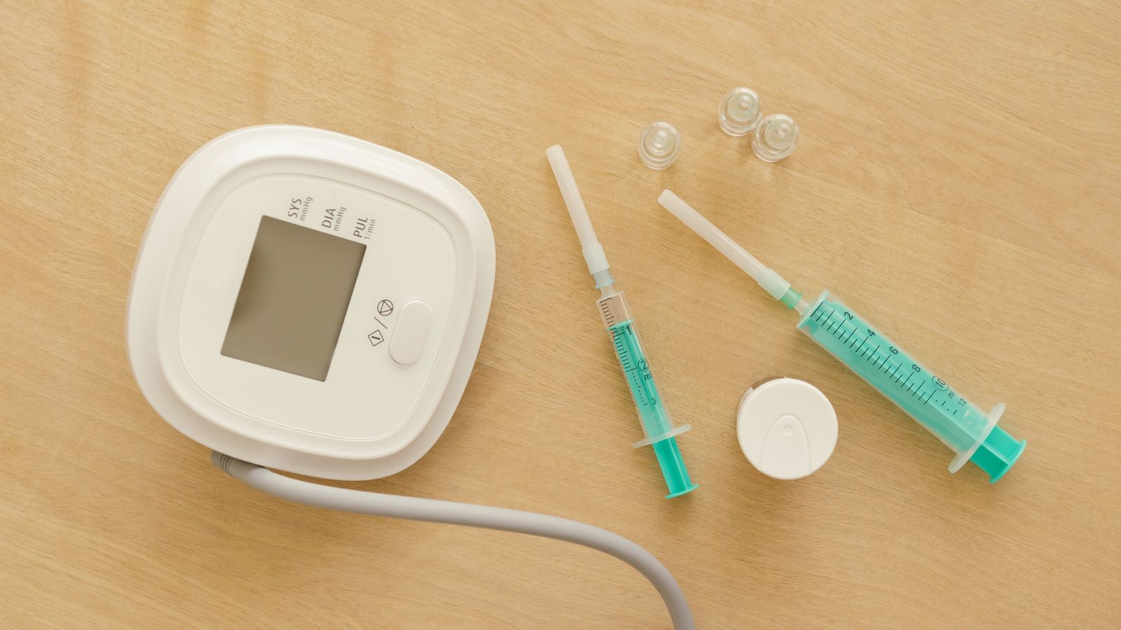 A sphygmomanometer and several syringes arranged on a wooden surface.