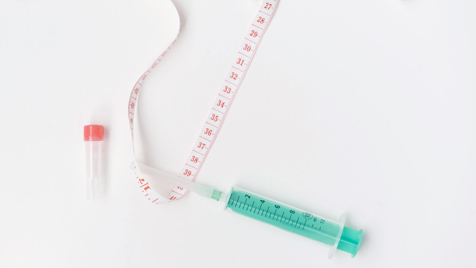 A tape measure and a syringe arranged flat on a white background alongside other medical supplies.