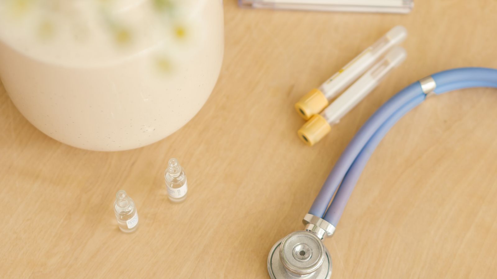 Stainless steel medical instruments and syringes laid out next to a stethoscope and small flowers on a table.